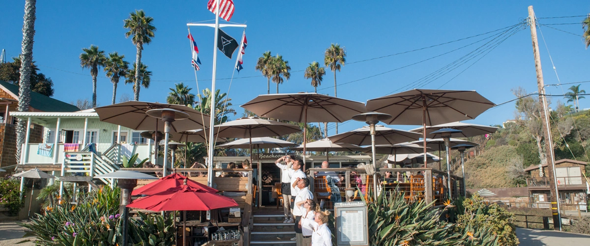Beachcomber staff saluting the flag on the entrance stairs beneath a bright blue sky.